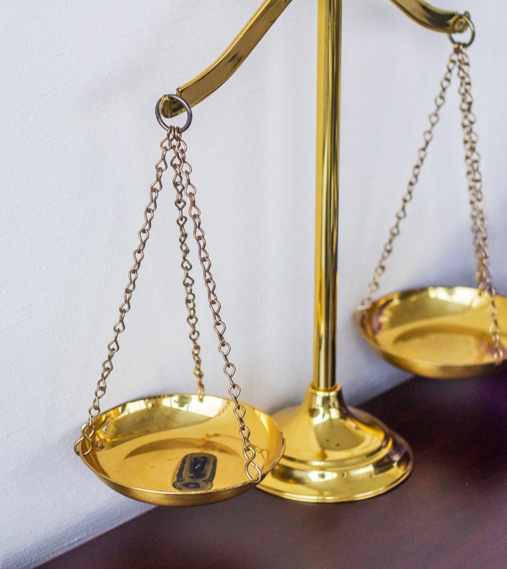 Photo of gold law scales on a brown desk.